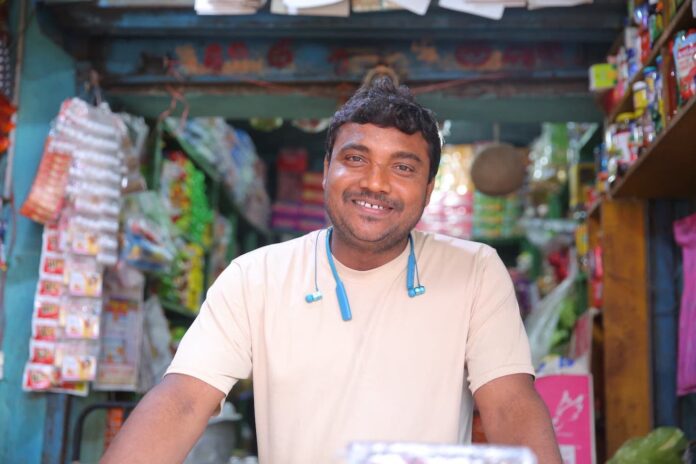 The Indian retail market is one of the largest in the world, with an estimated size of around INR 108 trillion as of 2022. The unorganized sector, which includes small kirana (grocery) stores, makes up about 88% of the total retail market. There are over 12 million kirana stores run by nano entrepreneurs across India, serving as the backbone of the grocery retail segment. There is an increasing need for these small-scale entrepreneurs to be part of the broader retail ecosystem, and this has started thanks to the training and mentorship offered to them by the government and private sector initiatives. Other factors like digital transformation, supportive government policies, improved logistics, access to financing, and adoption of technology also play a significant role in empowering these nano entrepreneurs. The Odisha Skill Development Authority’s ‘Swakalpa’ Project has transformed over 90 rural retail businesses in Odisha, including that of Mitu Nayak, an 8th-grade dropout from Astaranga, Odisha. He struggled as the sole provider for his family of seven with a modest grocery shop. Limited by basic amenities and a narrow market reach, he couldn’t stock high-demand items or expand beyond his immediate area. His earnings barely covered expenses. However, his fortune changed when he joined the Swakalpa program, a self-employment initiative by the Odisha Skill Development Authority and World Skill Center. Through 100 hours of mentorship, Mitu developed a robust business plan, gained market insights, and honed essential skills. Rebranding his store as “Maa Mangala Grocery Shop,” he enhanced its image, becoming a community hub. With newfound confidence and expertise, Mitu expanded his offerings, meeting community demands, and securing a brighter future. Swakalpa assisted Mitu with Udyam Aadhar registration and other legal compliances for his business. Following a growth strategy, Swakalpa also helped him tap into credit opportunities through the PM MUDRA scheme, securing a loan of INR 50,000. Mitu invested this loan to buy a commercial refrigerator, allowing him to expand his product range and supply more retailers in the locality. With this new equipment, he can stock multiple high-demand items for longer periods, especially in the summer, thus better meeting his customers’ needs. Through this strategy, he is able to serve the local market while also catering to other retail and wholesale markets. Additionally, he has reached out to large event vendors to supply products such as dry food and beverages for various events, opening a new market for his store. Mr. Amit Patjoshi, CEO, Palladium India, said “With Swakalpa’s help, Mitu focussed on adoption of technology to make operations efficient and attract more customers. He smoothened his supply chain and reduced delivery timelines by onboarding on the Hindustan Unilever’s (HUL’s) Shikhar mobile application. The store also allows digital payments to customers who do not want to pay cash. He has also adopted digital accounting using the Khatabook app for easy transactions and keeping track of finances.” With these interventions, over the past few months, Mitu has multiplied his average monthly turnover to about INR 7-10 lakhs. Looking ahead, his business projects a turnover of about INR 1 Cr for the upcoming year. He has hired three of his community members to manage his shop and business and is looking to set up a supermarket and create further job opportunities as his business expands. His business is attracting an average daily footfall of 150-200 customers, which includes both local shoppers & retailers.